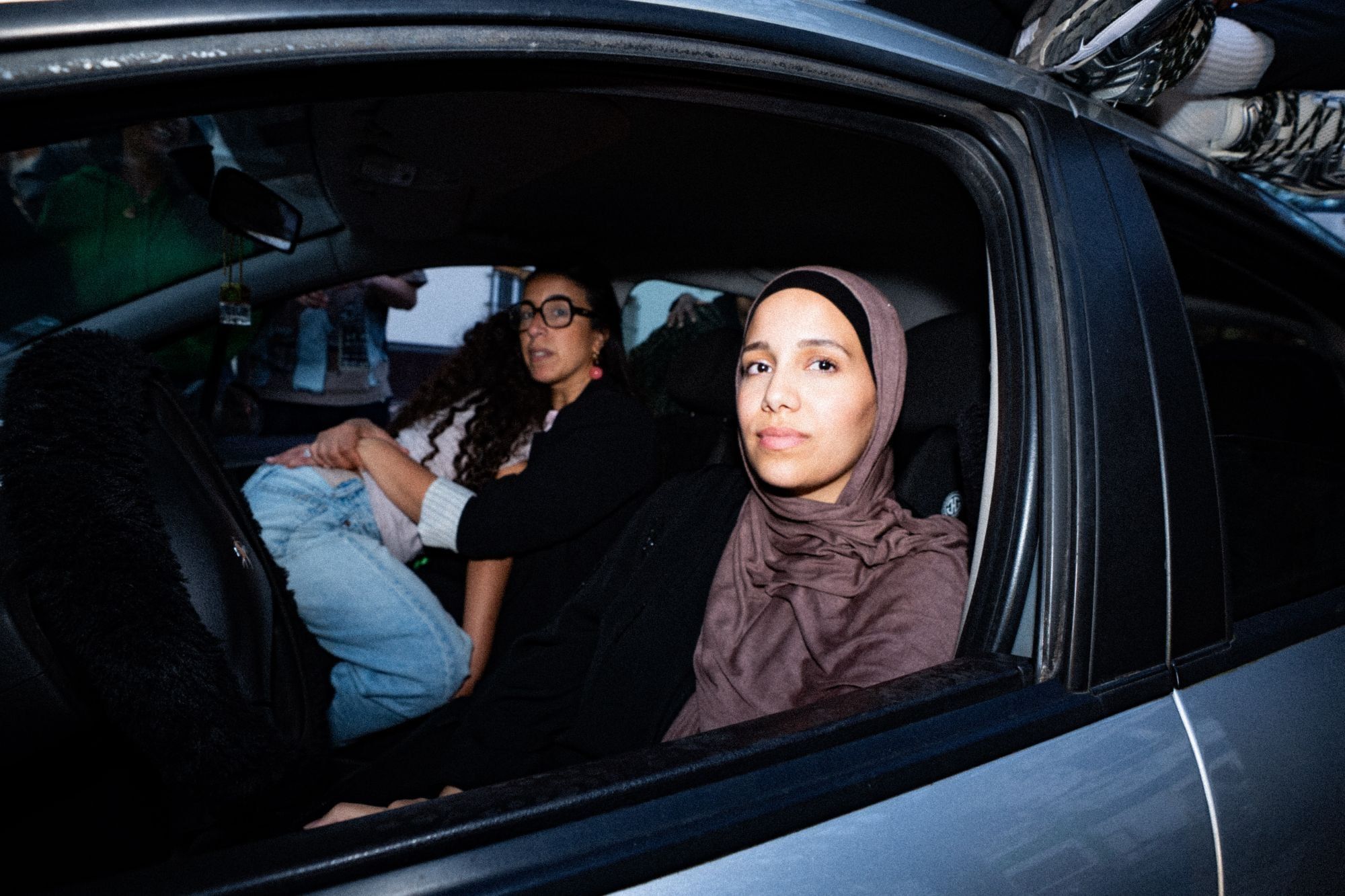 À l'intérieur d'une voiture, éclairées au flash, deux personnes assises à l'avant regardent vers l'objectif ; d'autres sont à peine visibles à l'arrière.